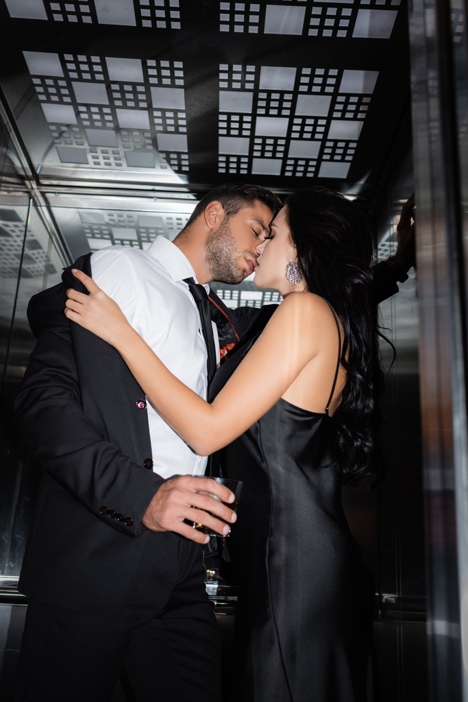 Молодая женщина раздевается парень со стаканом виски в лифте  - Фото, изображение