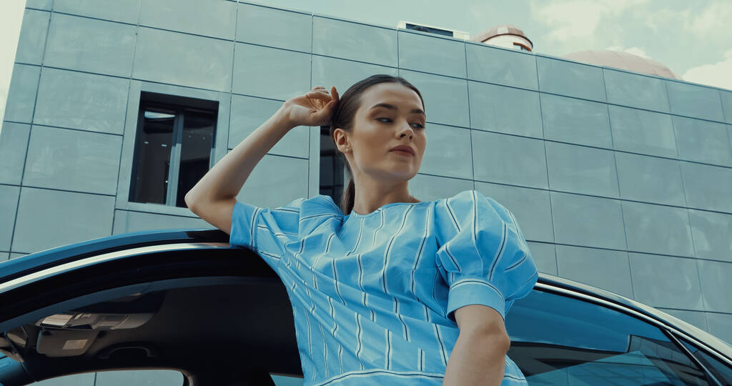 молодая брюнетка в синей блузке позирует возле машины - Фото, изображение