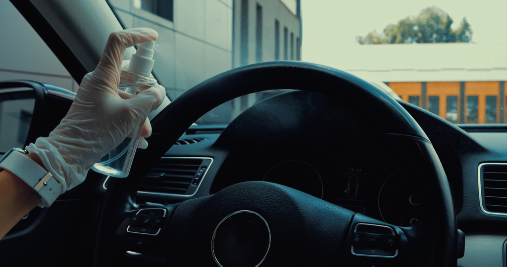 bijgesneden beeld van vrouw in latex handschoen sproeien ontsmettingsmiddel op stuurwiel in auto - Foto, afbeelding
