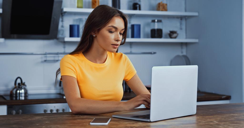 fiatal nő használ laptop közelében okostelefon üres képernyőn - Fotó, kép