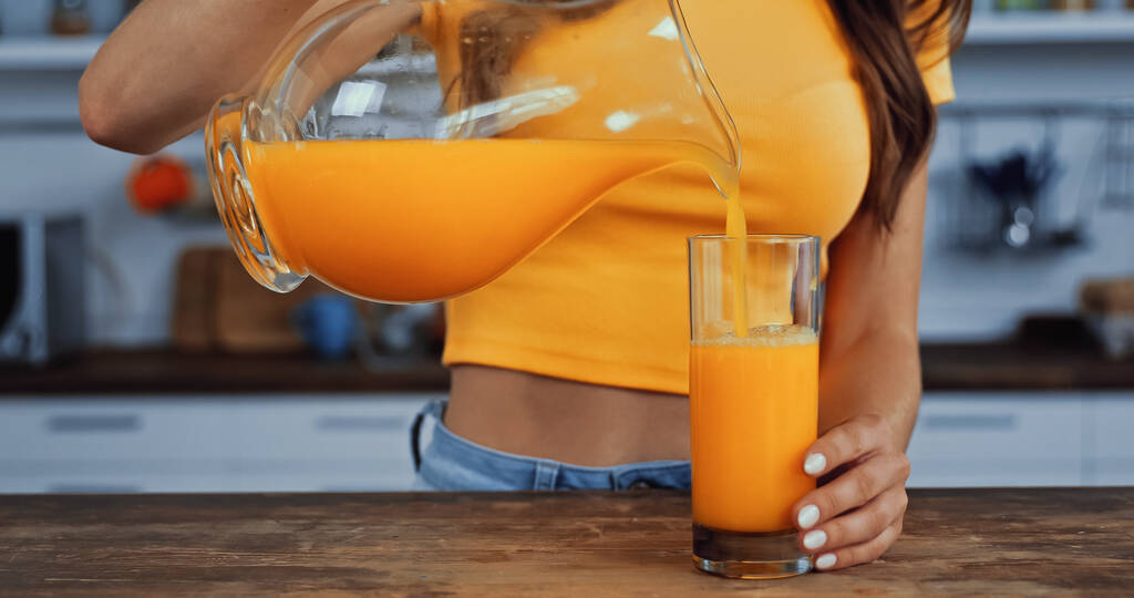 καλλιεργημένη άποψη της νεαρής γυναίκας χύνοντας χυμό πορτοκαλιού σε ποτήρι - Φωτογραφία, εικόνα