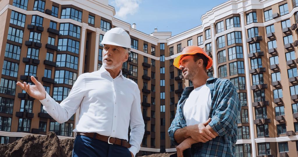Низкий угол обзора инженера жестом рядом со строителем, разговаривая рядом с новым зданием - Фото, изображение