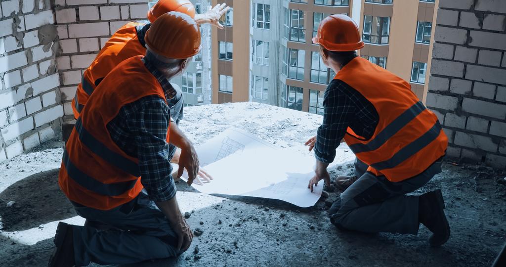 builders in hand hats discussing blueprint while sitting on construction site - Photo, Image
