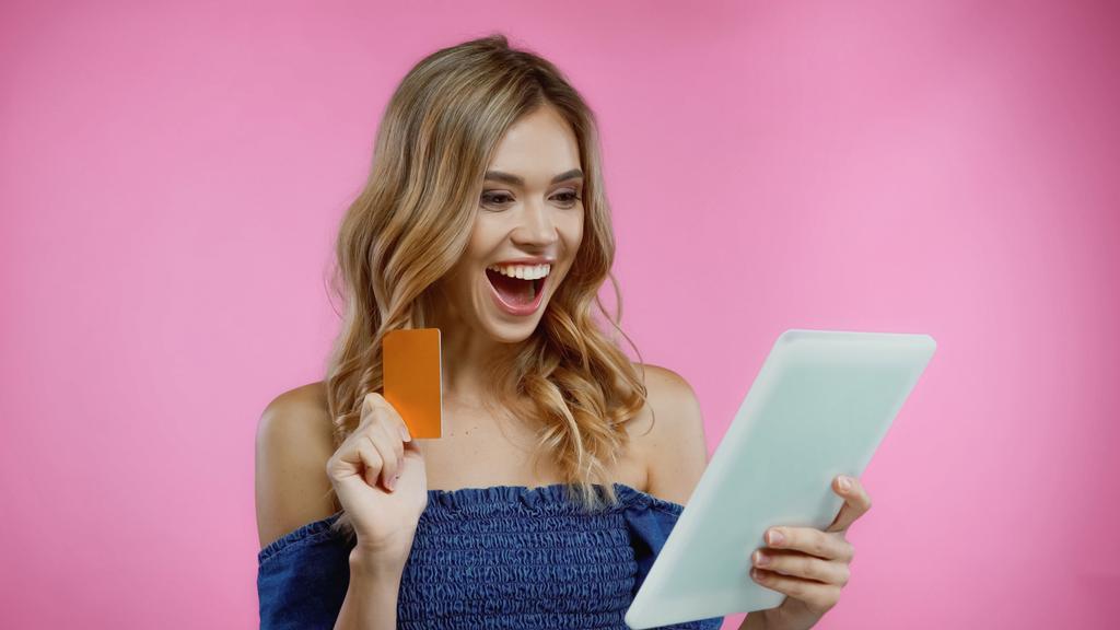mujer sorprendida sosteniendo tarjeta de crédito y tableta digital aislado en rosa - Foto, Imagen