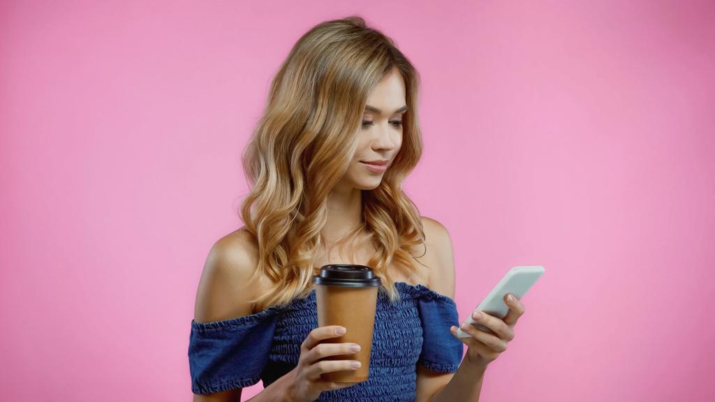 Blondi nainen käyttää älypuhelinta ja pitämällä kahvia mennä eristetty vaaleanpunainen - Valokuva, kuva