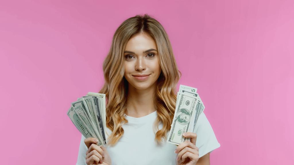 allegra giovane donna in t-shirt bianca con dollari isolati su rosa - Foto, immagini
