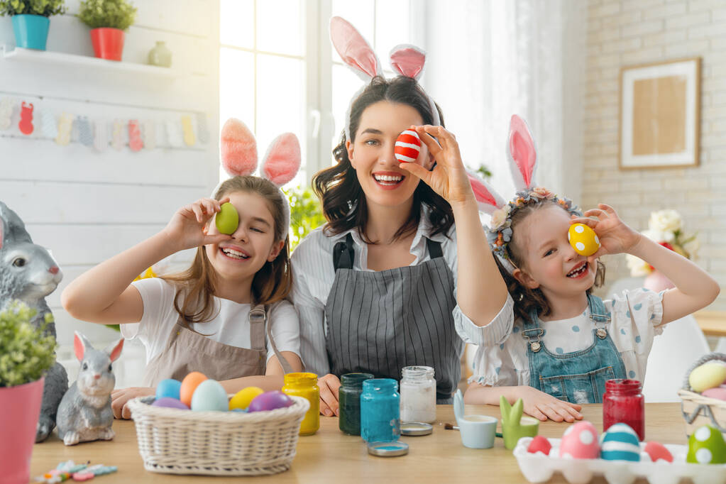 Šťastnou dovolenou! Matka a její dcery malují vejce. Rodina se připravuje na Velikonoce. Roztomilé malé děti dívky nosí králičí uši. - Fotografie, Obrázek