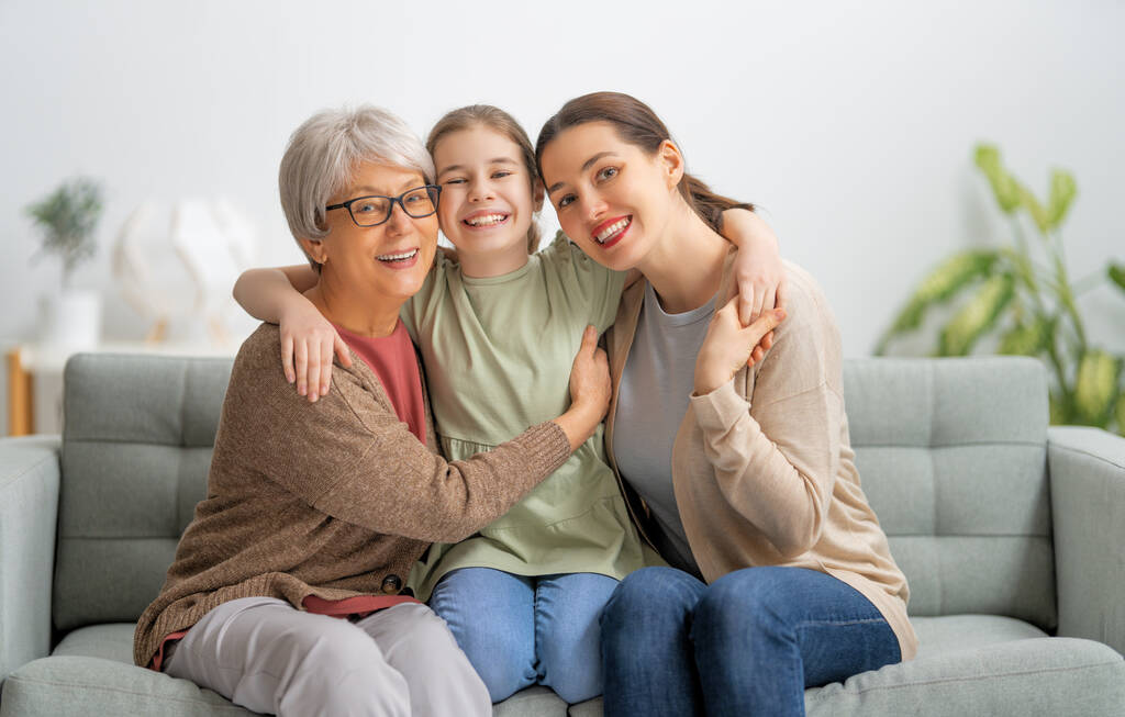 Uma menina agradável, sua mãe e avó estão abraçando e gostando de passar o tempo juntos em casa.  - Foto, Imagem