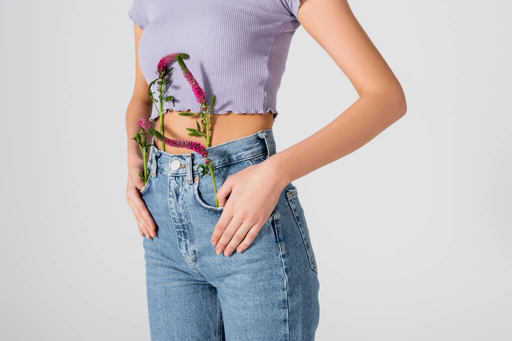 vista recortada de mujer joven en jeans con flores de altramuz en bolsillos posando aislados en blanco  - Foto, imagen