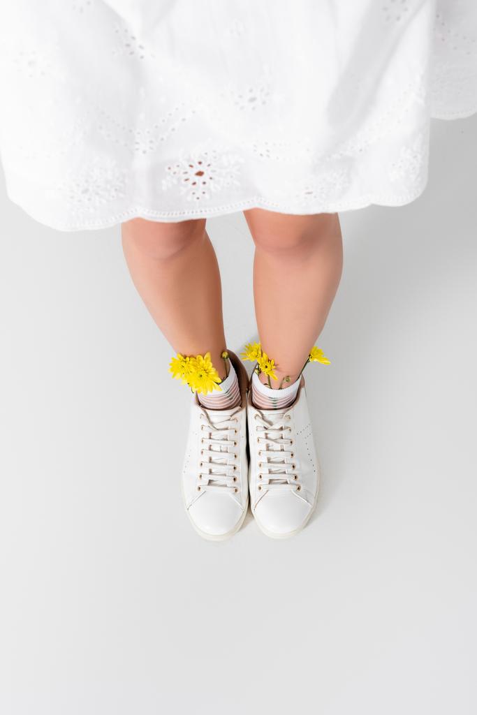 high angle view of model in sneakers with yellow spring wildflowers posing on white - Photo, Image