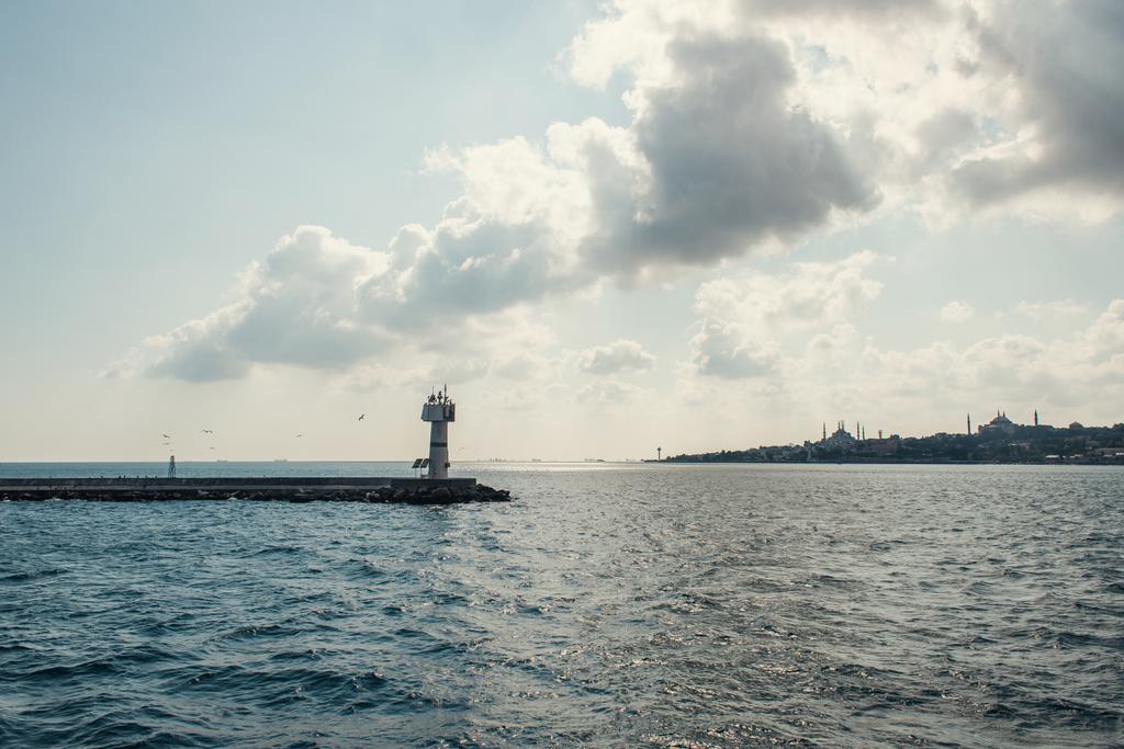 Latarnia morska na molo na morzu i zachmurzone niebo na tle Stambułu, Turcja  - Zdjęcie, obraz