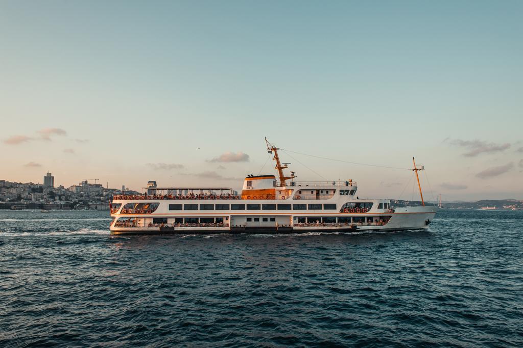 Πλοίο σε θαλάσσια ύδατα με ακτή και πόλη στο βάθος κατά τη διάρκεια του ηλιοβασιλέματος, Κωνσταντινούπολη, Τουρκία  - Φωτογραφία, εικόνα