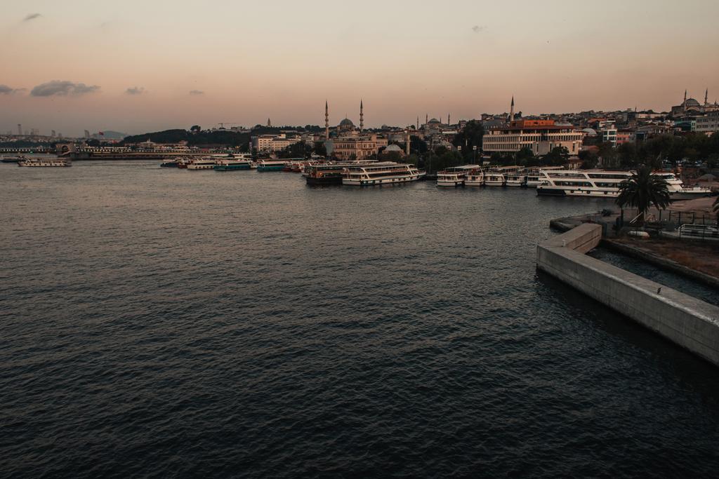 Barcos con agua de mar y edificios en la costa de Estambul al atardecer, Turquía  - Foto, imagen