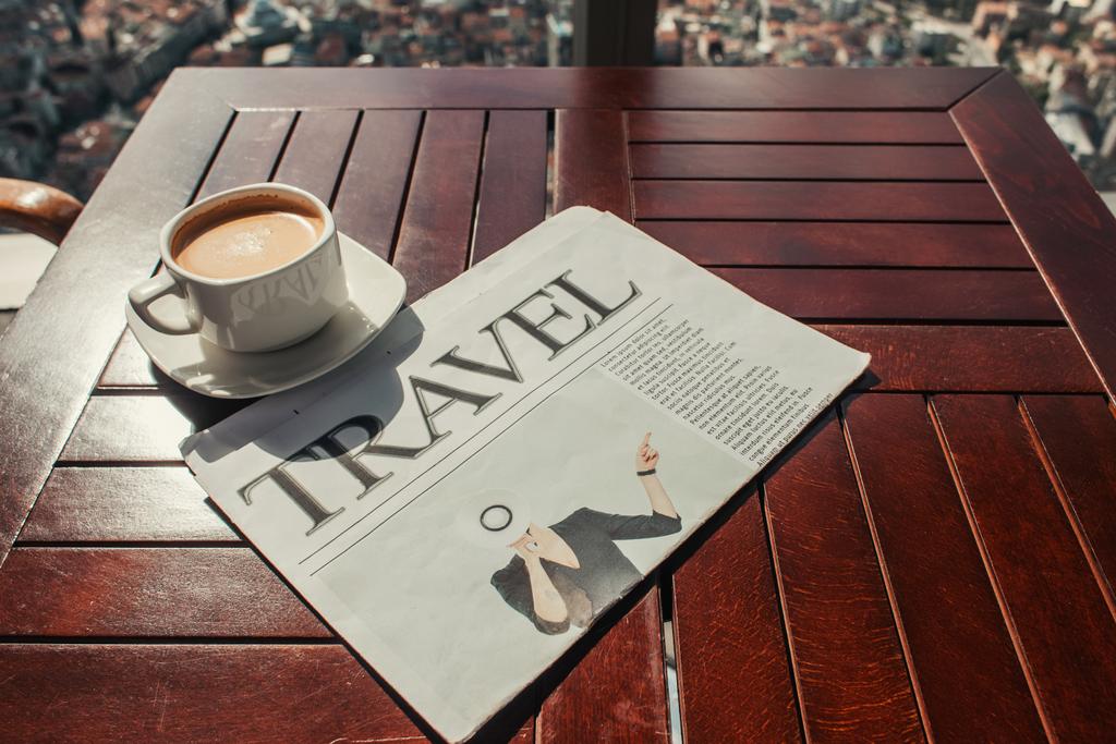 φλιτζάνι καφέ και ταξιδιωτική εφημερίδα σε ξύλινο τραπέζι στο καφέ  - Φωτογραφία, εικόνα