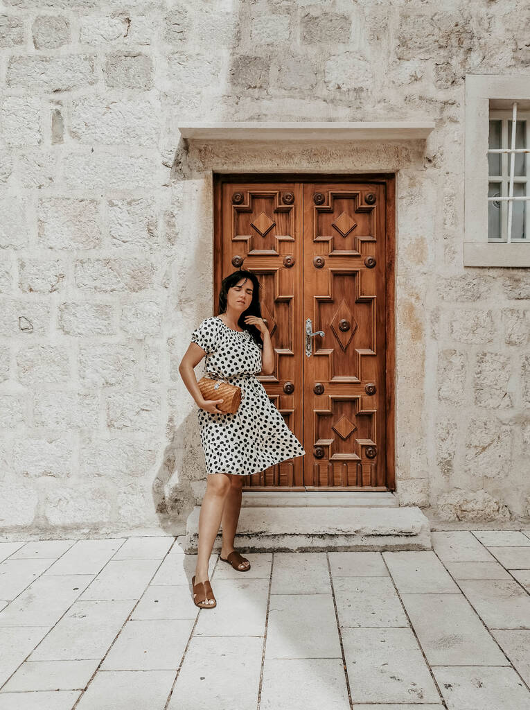 A confident Caucasian woman in a polka-dotted flowy dress posing against a decorative old door - Photo, Image