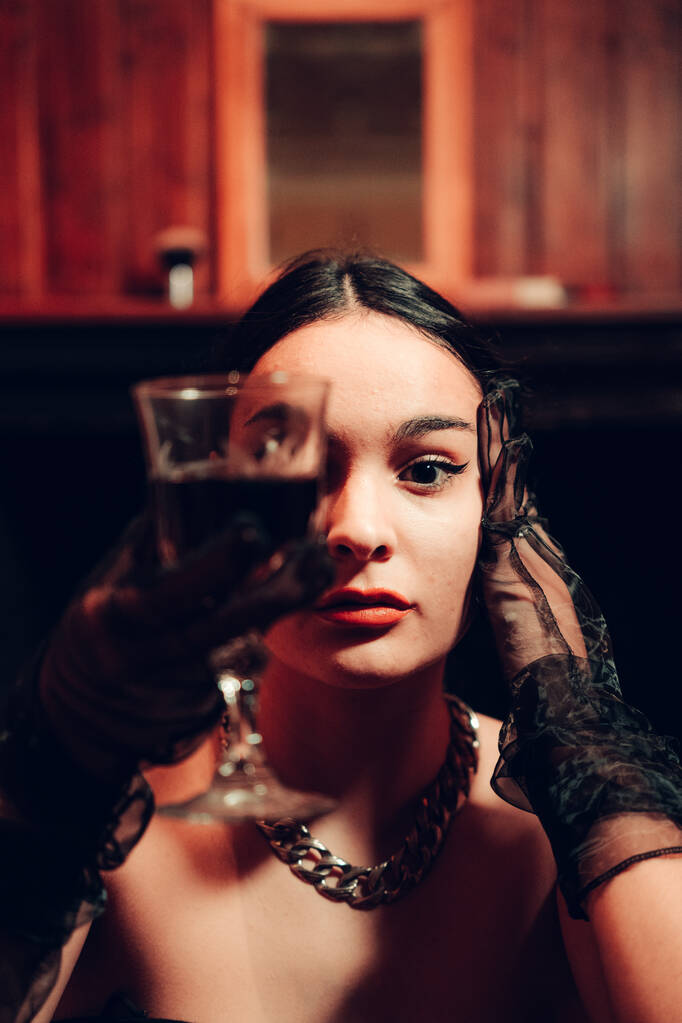 Porträt einer jungen sexy Frau mit einem Glas Rotwein und langen modischen Handschuhen in einem künstlich beleuchteten Raum - Foto, Bild