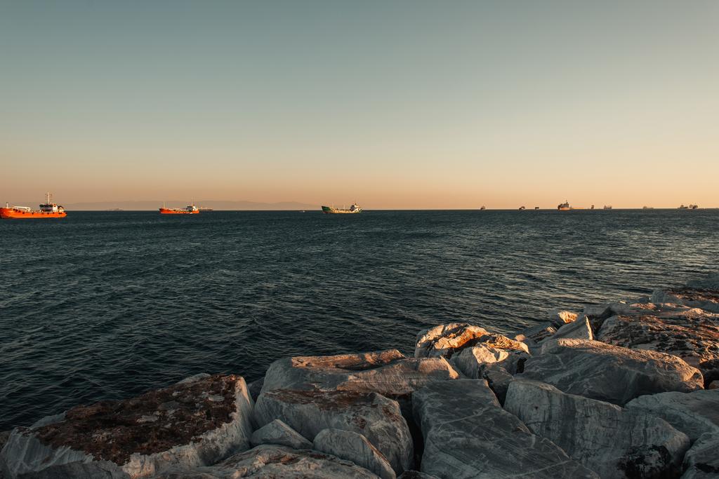 wolkenloze lucht boven schepen op zee, en stenen zeekust - Foto, afbeelding