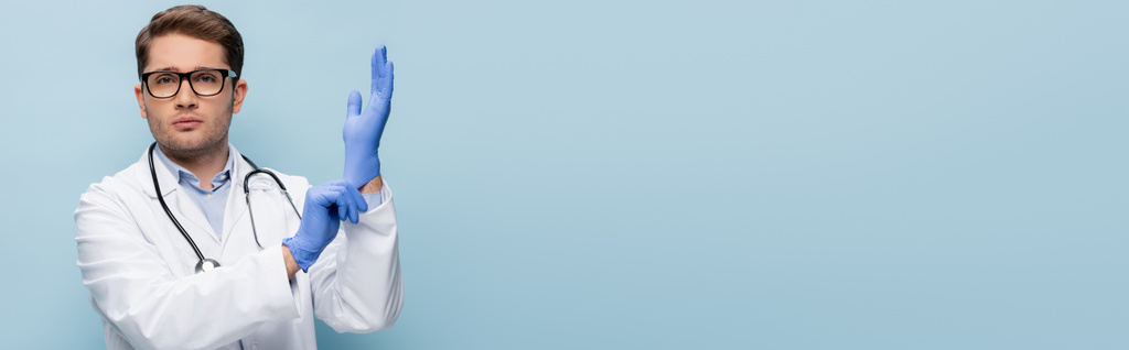 doctor in glasses and white coat wearing latex gloves isolated on blue, banner - Photo, Image