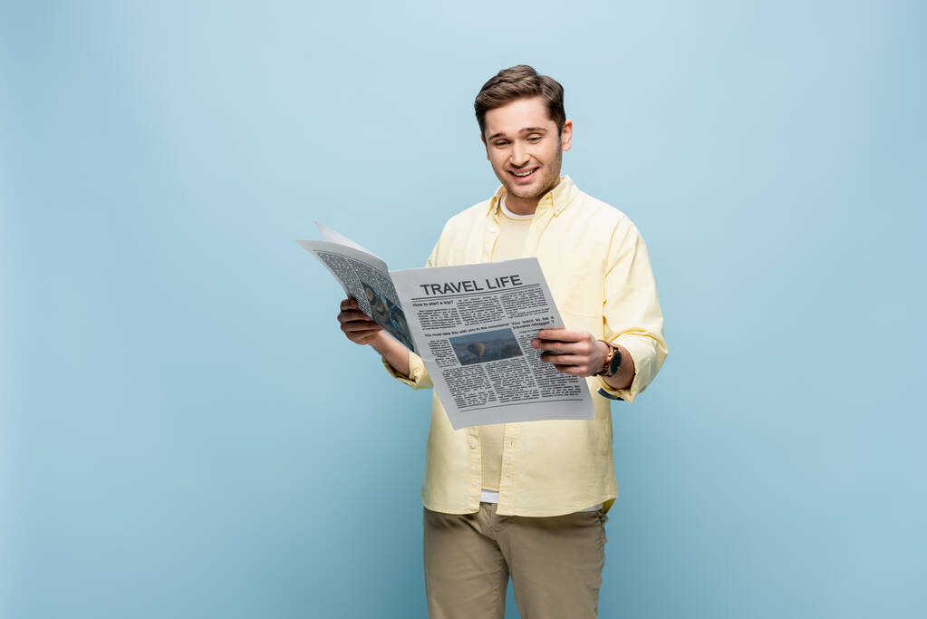 χαρούμενος νεαρός άνδρας με πουκάμισο διαβάζει ταξιδιωτική εφημερίδα στο μπλε - Φωτογραφία, εικόνα
