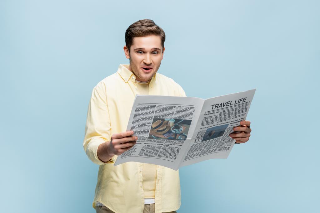 surprised young man in shirt reading travel newspaper isolated on blue - Photo, Image