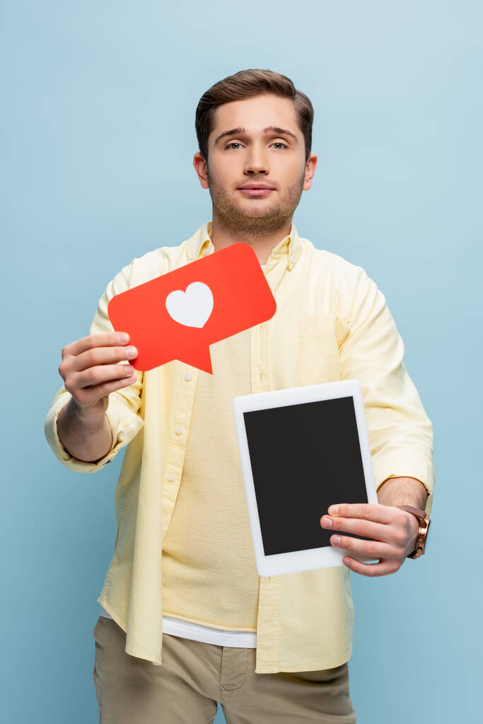 muž v košili drží papírové srdce a digitální tablet s prázdnou obrazovkou izolované na modré - Fotografie, Obrázek