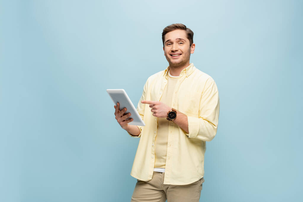 fröhlicher Mann im gelben Hemd zeigt mit dem Finger auf digitales Tablet - Foto, Bild