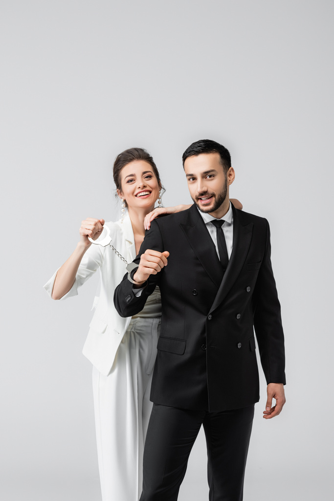 Mariée joyeuse en voile tenant les menottes du petit ami arabe isolé sur gris  - Photo, image
