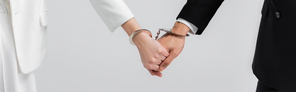 Widok nowożeńców trzymających się za ręce w kajdankach odizolowanych na szarym, szarym transparencie  - Zdjęcie, obraz