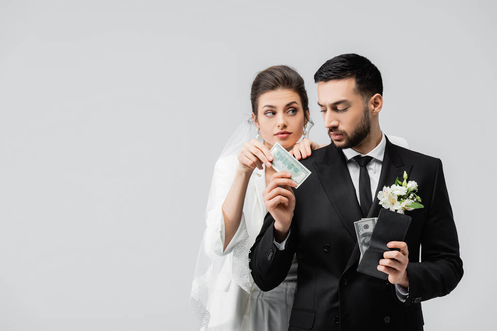 Lo sposo musulmano tiene il portafoglio e dà banconote in dollari alla sposa isolata su grigio  - Foto, immagini