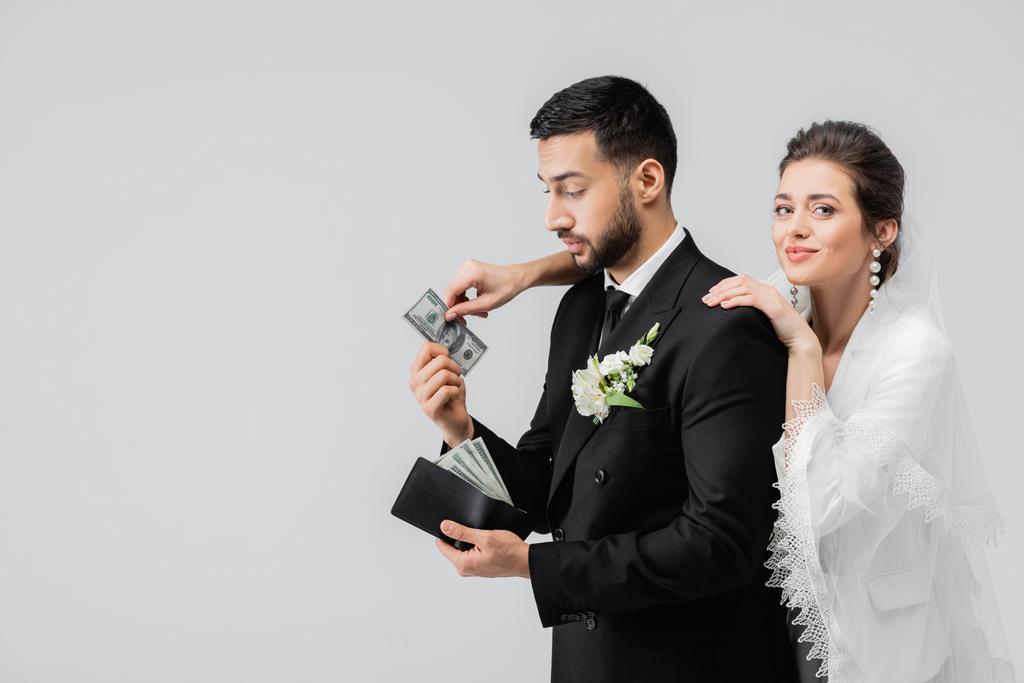 Sposa sorridente che prende valuta da sposo musulmano isolato su grigio  - Foto, immagini