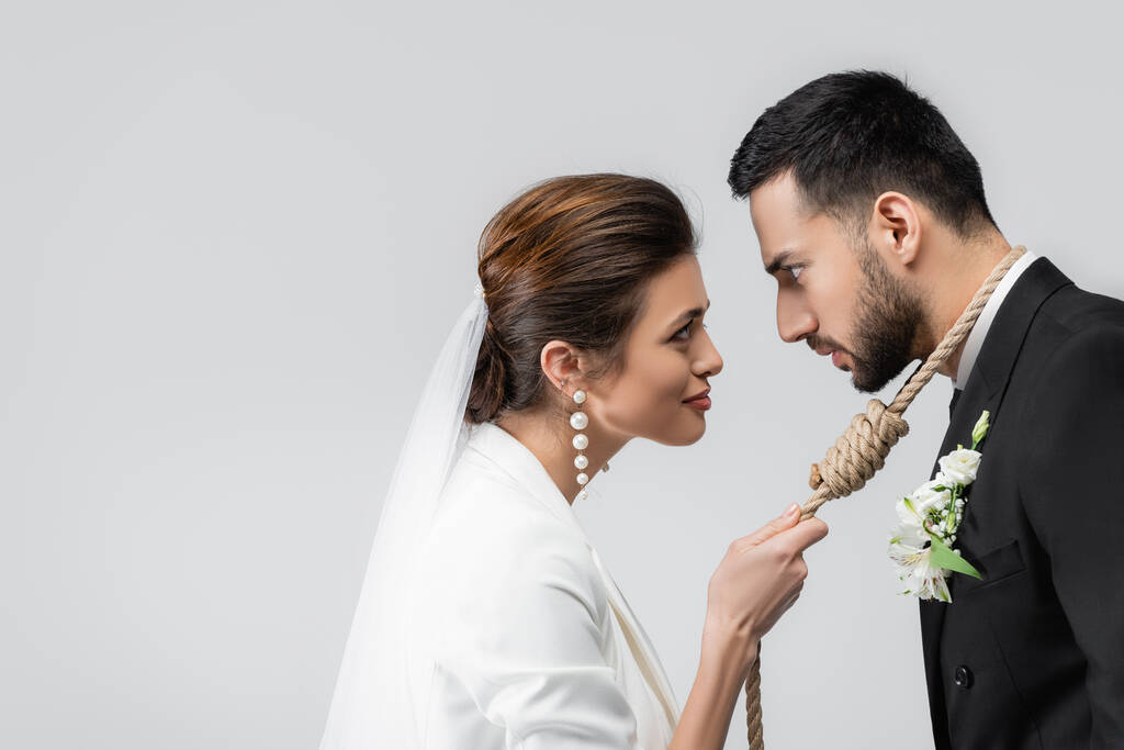 Πλευρική άποψη του αραβικού γαμπρού με κόμπο ολίσθησης στο λαιμό κοιτάζοντας τη νύφη που απομονώνονται σε γκρι  - Φωτογραφία, εικόνα