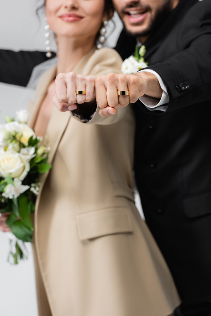vista parcial de la pareja recién casada mostrando anillos de boda sobre fondo borroso aislado en gris - Foto, imagen