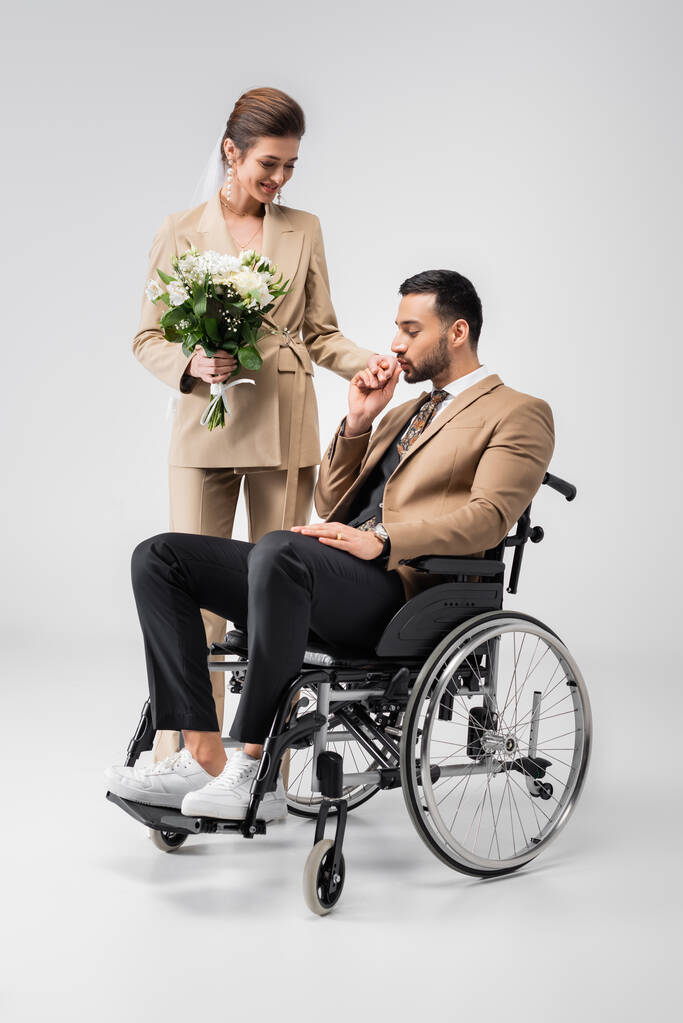 handicapped muslim man kissing hand of happy bride holding wedding bouquet on grey - Photo, Image