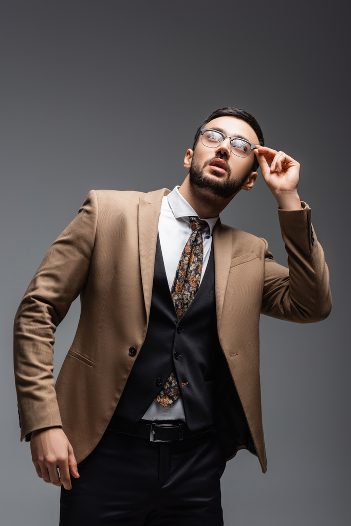 homme arabe à la mode ajustant les lunettes tout en levant les yeux sur le gris - Photo, image
