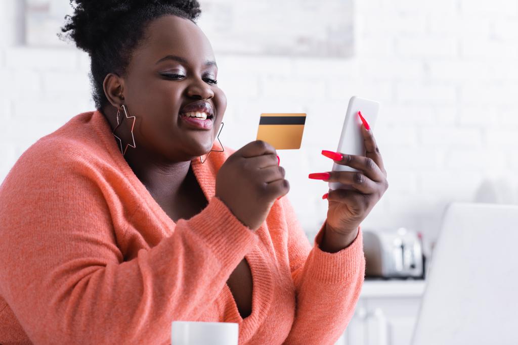 sorridente afro americano plus size donna in possesso di carta di credito e telefono cellulare - Foto, immagini