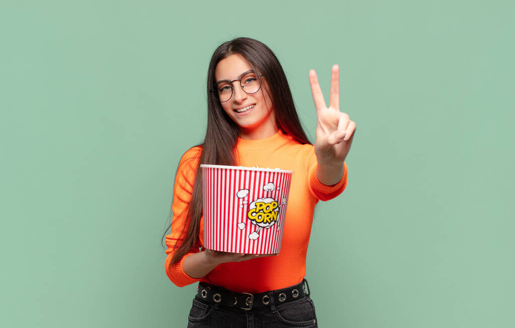 young pretty woman smiling and looking friendly, showing number two or second with hand forward, counting down. pop corns concept - Photo, Image