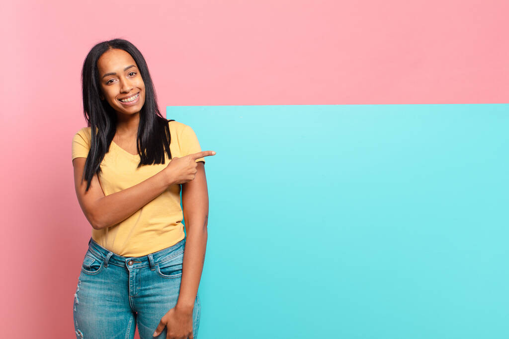 若い黒人女性は陽気に笑って幸せを感じ横と上を指差してコピースペースに物を見せる。コピースペースのコンセプト - 写真・画像