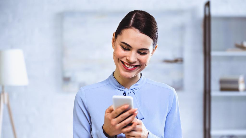 šťastná podnikatelka se usmívá, zatímco chatuje na smartphone v kanceláři - Fotografie, Obrázek