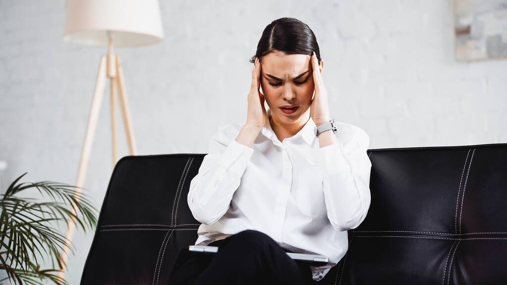 donna d'affari esausta che soffre di mal di testa mentre è seduta sul divano con il computer portatile - Foto, immagini