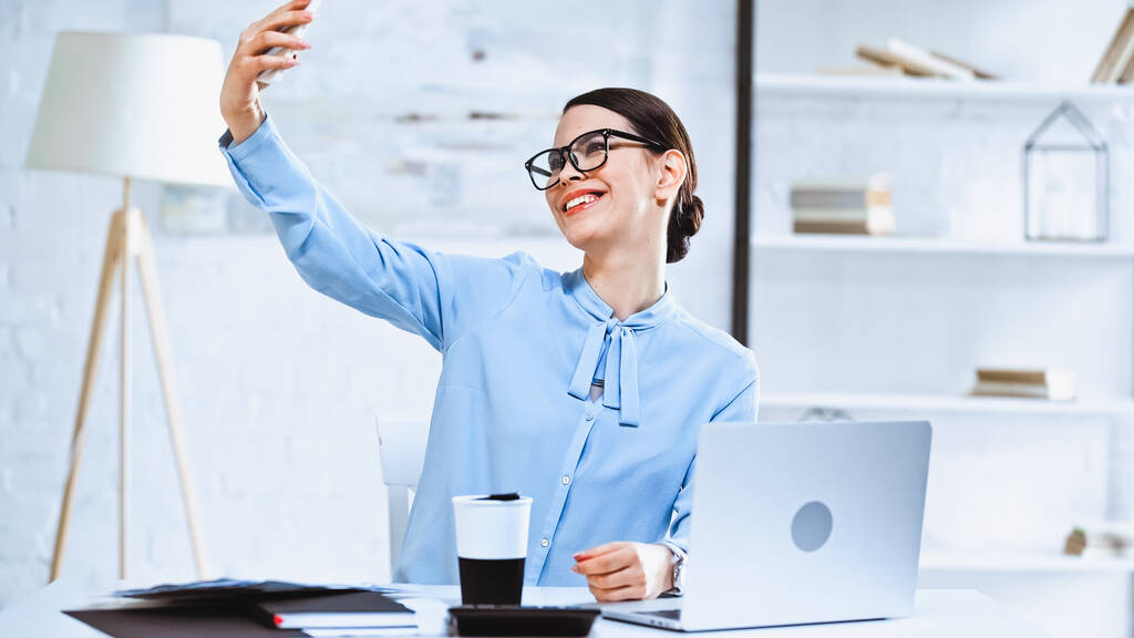cheerful businesswoman taking selfie on smartphone in office - Photo, Image