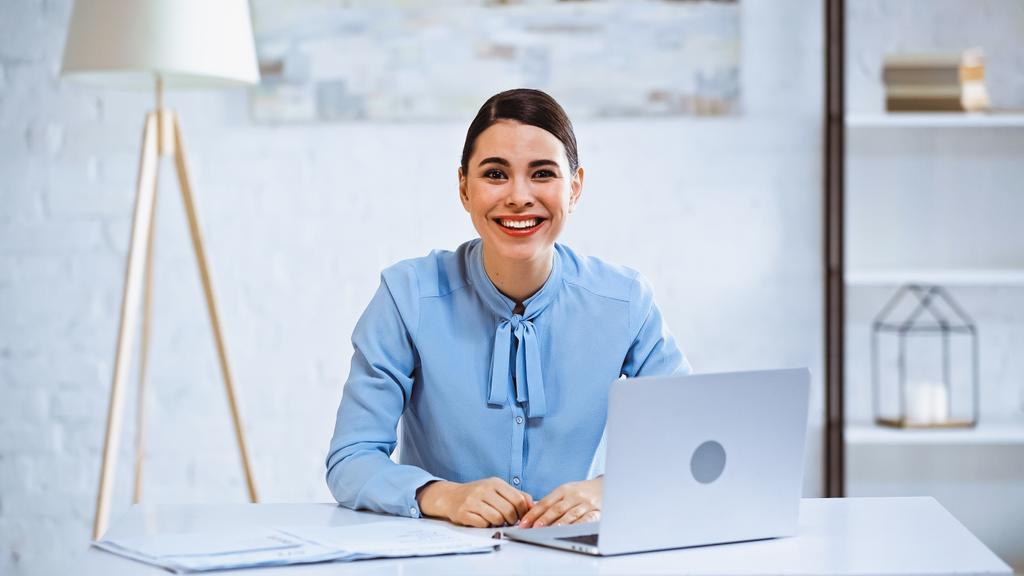 glückliche Geschäftsfrau lächelt in die Kamera, während sie am Arbeitsplatz im Büro sitzt - Foto, Bild