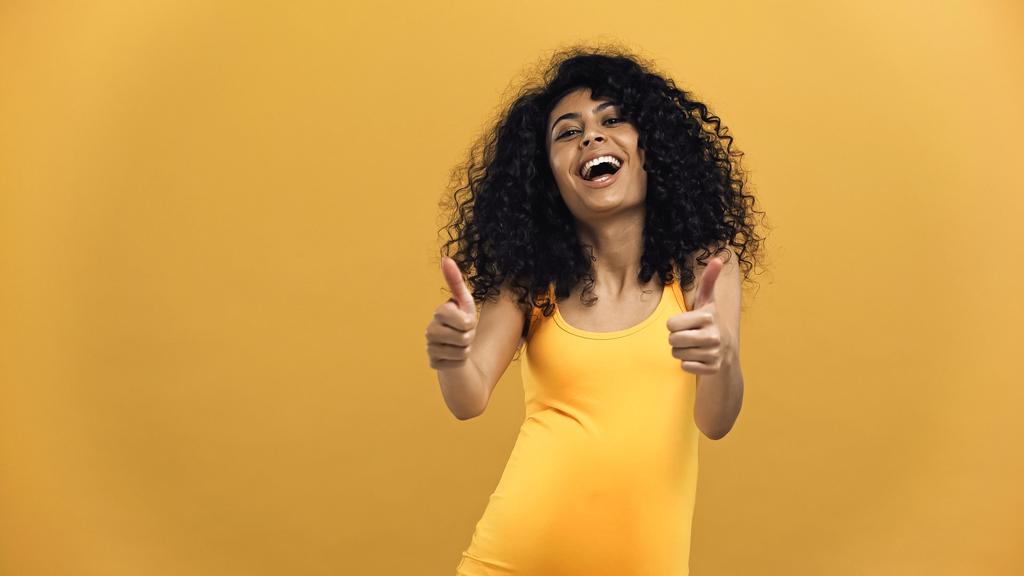 陽気妊娠中のヒスパニック女性ショー親指アップ絶縁上の黄色 - 写真・画像