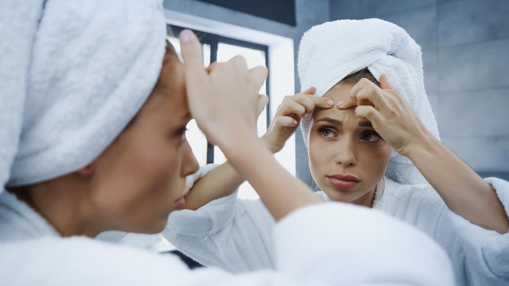 besorgte junge Frau quetscht Pickel und blickt im Badezimmer in den Spiegel - Foto, Bild