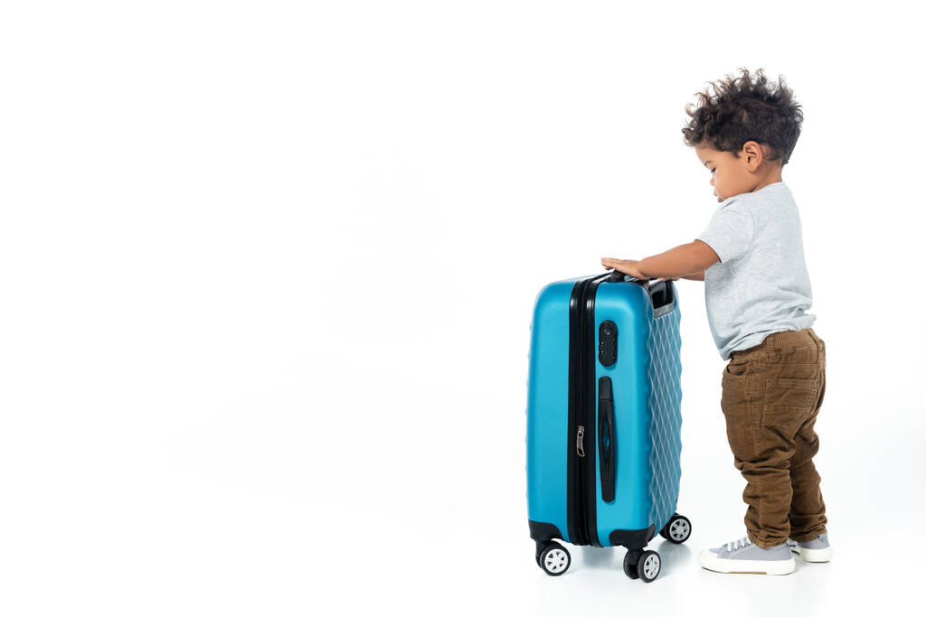 plná délka pohled batole africký americký chlapec stojící v blízkosti cestovní taška na bílém - Fotografie, Obrázek