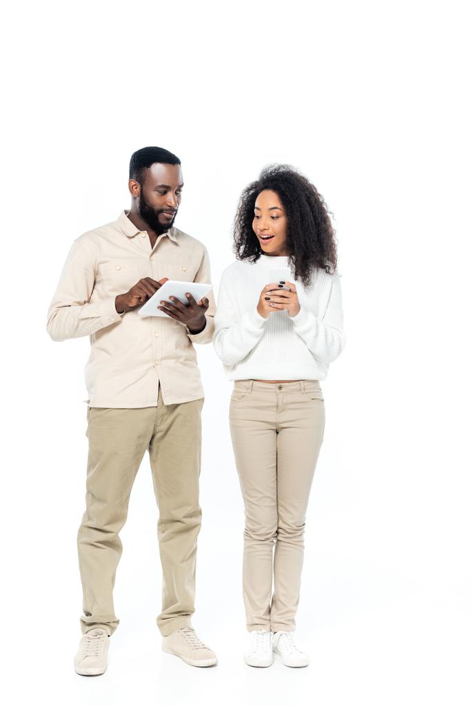 здивована афроамериканська жінка тримає смартфон, дивлячись на цифровий планшет в руках чоловіка на білому
 - Фото, зображення