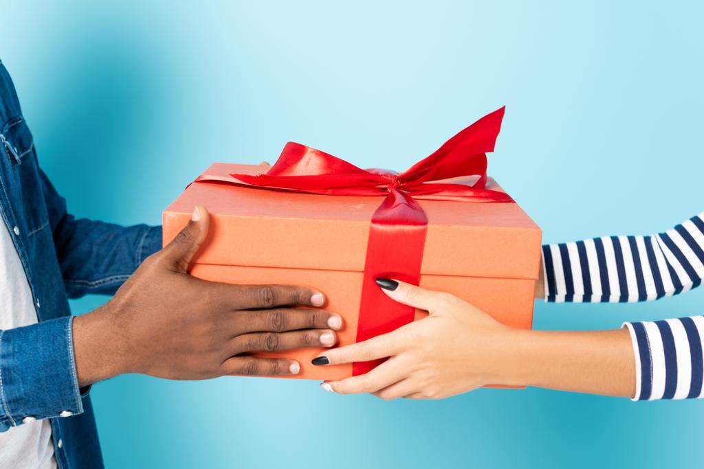 abgeschnittene Ansicht eines afrikanisch-amerikanischen Ehepaares mit Geschenkbox auf blauem Grund - Foto, Bild