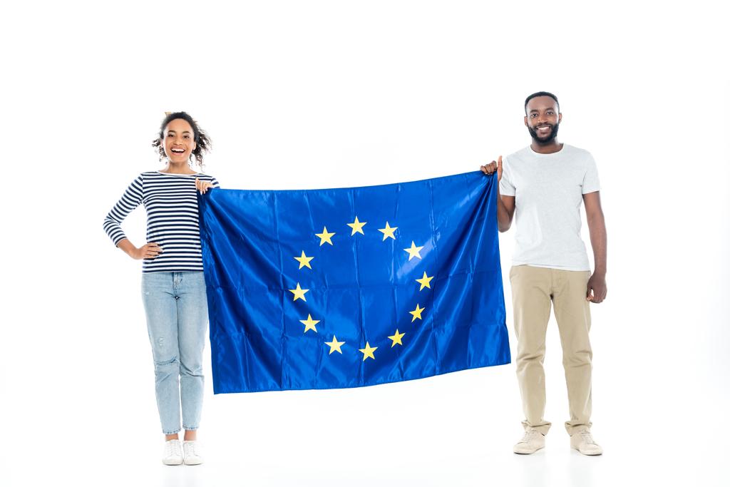 młoda afrykańska para uśmiecha się do kamery trzymając flagę Unii Europejskiej na białym tle - Zdjęcie, obraz