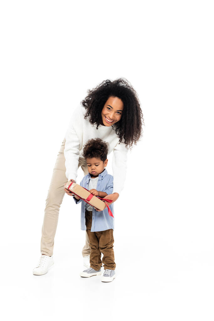 alegre africano americano mujer mirando cámara cerca hijo con regalo caja en blanco - Foto, imagen