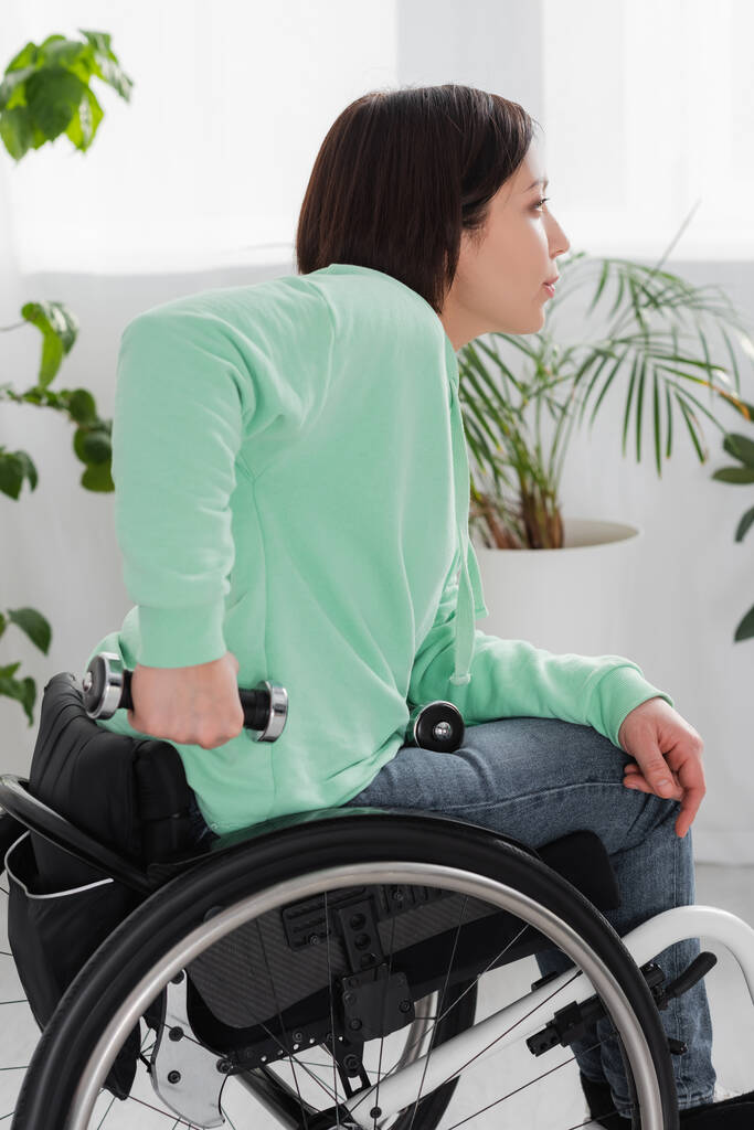 Πλευρική άποψη της γυναίκας άσκηση με αλτήρα σε αναπηρικό αμαξίδιο  - Φωτογραφία, εικόνα