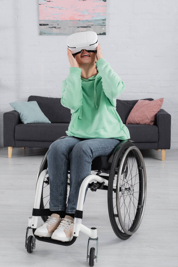 Donna sorridente in sedia a rotelle utilizzando cuffie realtà virtuale  - Foto, immagini